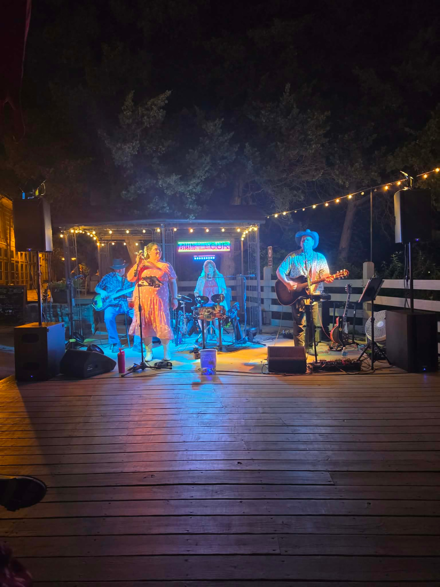 Full band performing on an outdoor stage at night under string lights